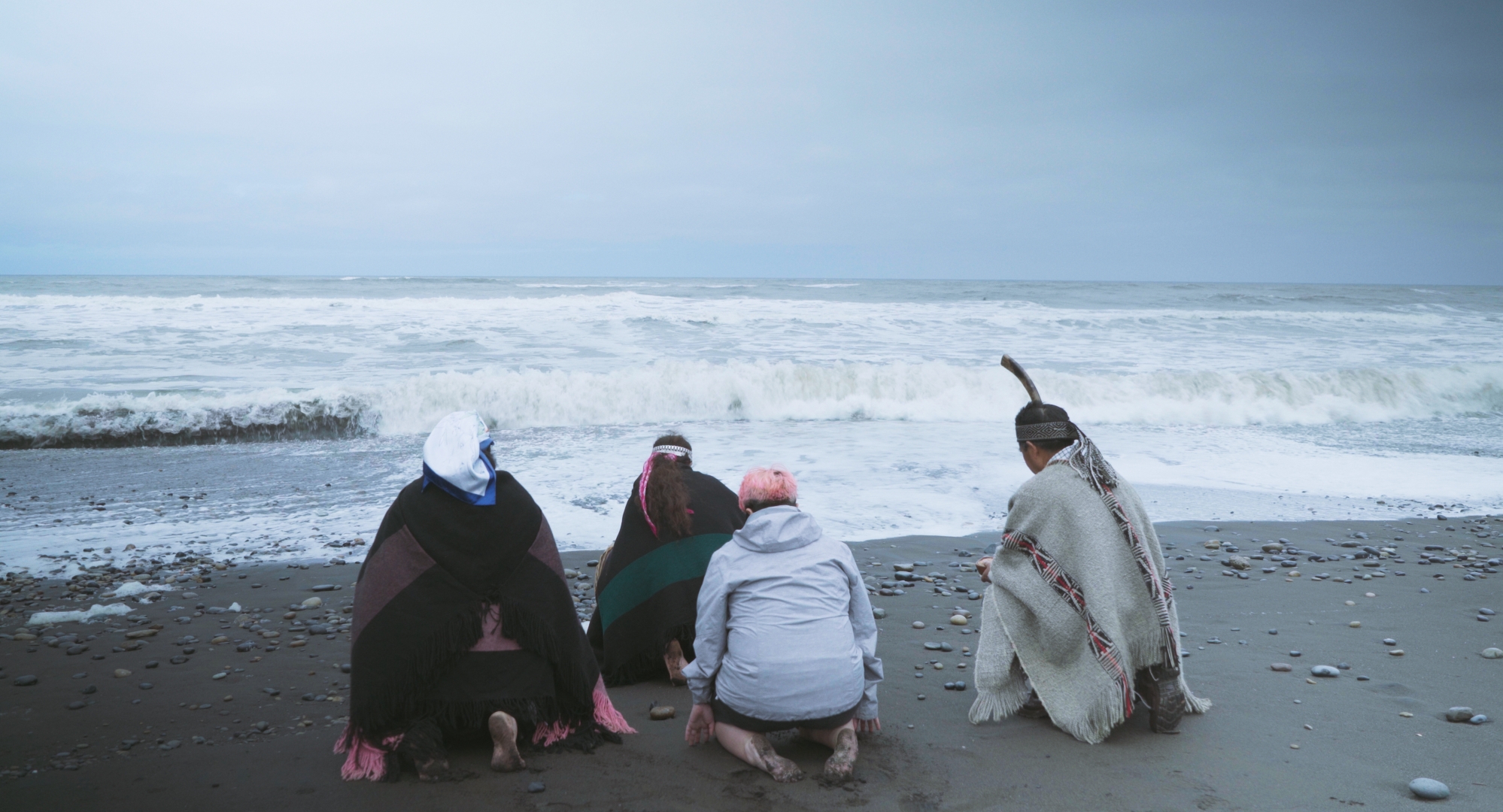 Cuatro personas, tres de ellas mapuche, hacen una ceremonia arrodilladas frente al mar.